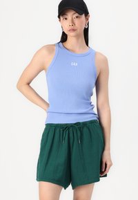 Top in cotone azzurro chiaro a coste con il logo "GAP"; abbinato a pantaloni corti verdi con cordino. Entrambi i capi presentano una vestibilità comoda e una texture morbida.