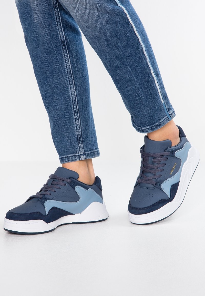 Chaussures de sport en cuir et matériaux synthétiques de couleur bleu foncé et bleu clair, avec un bout perforé, des accents texturés et des semelles blanches.
