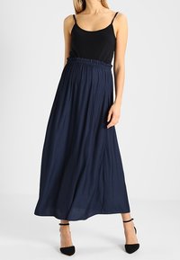 Maxi sukně v námořnické modři, vyrobená z lehkého materiálu, s elastickým pasem. V kombinaci s přiléhavým černým topem bez rukávů a podpatky.