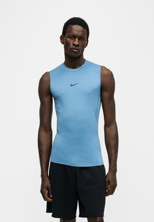 Homme athlétique portant un haut Nike bleu moulant sans manches et un short noir ample, debout devant un fond clair uni.