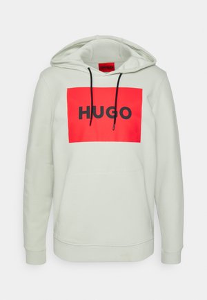 Jasnoszara bluza z kapturem z czerwonym prostokątnym logo z napisem „HUGO” czarnymi literami i czarnymi sznurkami przy kapturze.