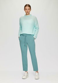 Lichtblauwe gebreide trui met een hoge hals, gedragen met teal tapered broeken en witte sneakers, voorzien van een drawstring taille en zijzakken.