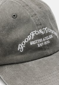 Szara bawełniana czapka z haftowanym białym napisem "GOOD FOR NOTHING BRITISH ATELIER EST 2011", z wyraźnym, sztywnym krojem.