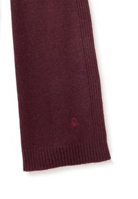 Burgundská pletená šála s žebrovanou texturou a malým vyšitým logem. Má měkký materiál s hladkým povrchem.