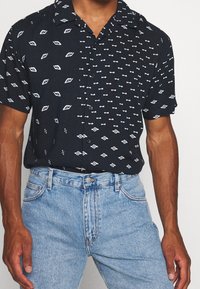 Kortärmad skjorta i svart med vita geometriska mönster. Mjuk, lätt tyg; kombinerad med högmidjade blå denimjeans.