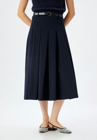 Gonna plissettata blu navy con vita aderente e una cintura nera. Il tessuto sembra liscio e le pieghe si estendono dalla vita all'orlo.