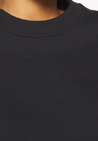 Sudadera negra con un cuello redondo acanalado y tejido texturizado. La vista en primer plano resalta el material suave y liso.