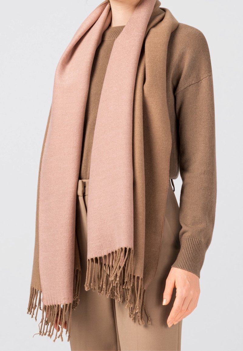 Pull en laine marron associé à une écharpe en laine rose clair avec des bords effilochés. L'écharpe se drape élégamment sur les épaules.