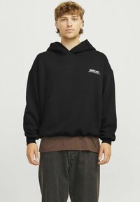 Zwarte hoodie met een voorzak en de opdruk "CREATIVE DEPT.". Het heeft een relaxed fit met geribbelde boorden, gelaagd over een bruine top.