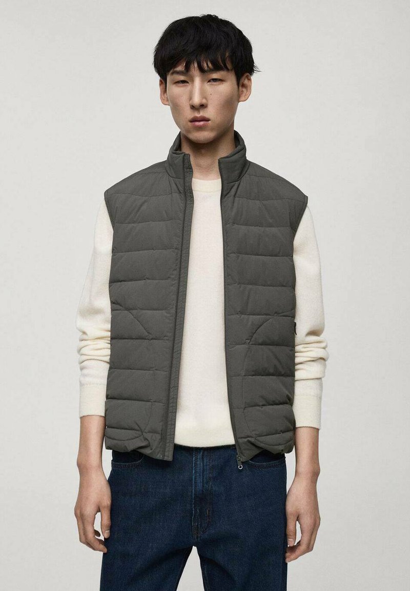 Grå kviltad väst med hög krage, ärmlös design och framzip. Bärs över en ljus tröja och tillsammans med mörka jeans.