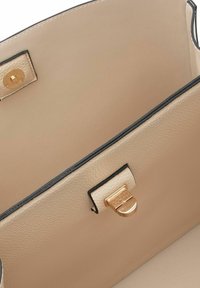 Bolso de mano de cuero beige con superficie texturizada, ribete negro, herrajes dorados y cierre con broche. El interior muestra un forro liso.