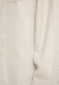 Beige knappskjorta i mjukt tyg, med en subtil strukturerad mönster och en broderad logotyp på fickan.