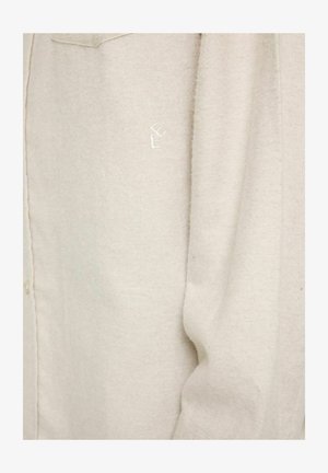 Beige skjorte med knapper lavet af blødt stof, med et subtilt tekstureret mønster og et broderet logo på lommen.