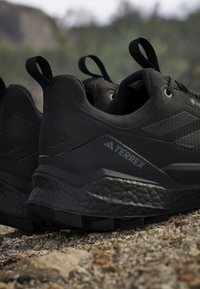 Coppia di scarpe da trail running nere Adidas Terrex su terreno roccioso con suola con texture visibile e linguette per facilitare la calzata.