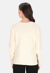 Krém színű kötött pulóver, chevron mintával, széles ujjakkal és kerek nyakkivágással, puha és texturált anyagból készült.