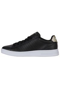 Baskets en cuir noir avec une semelle en caoutchouc blanche, présentant de subtiles rayures verticales et une finition métallique dorée au talon. Lacets et œillets noirs.