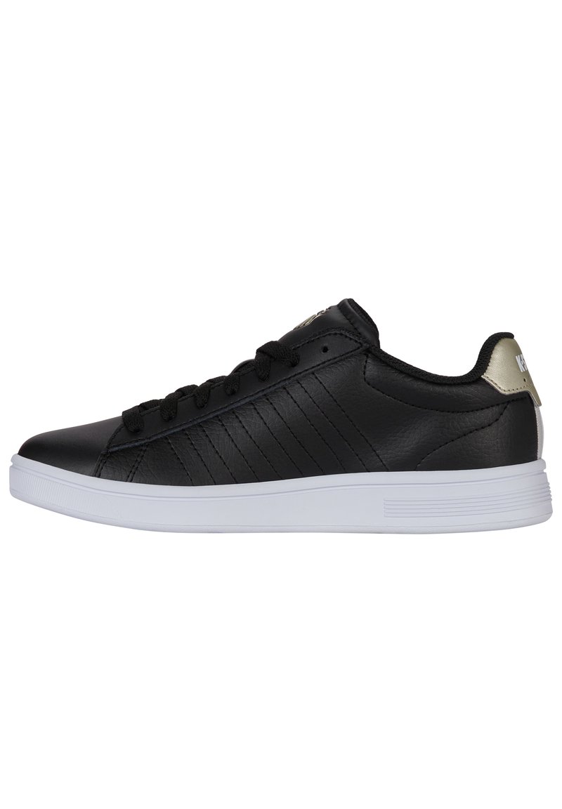 Baskets en cuir noir avec une semelle en caoutchouc blanche, présentant de subtiles rayures verticales et une finition métallique dorée au talon. Lacets et œillets noirs.
