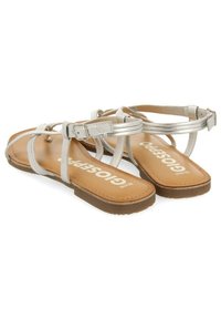Sandalias planas metálicas plateadas con correas delgadas, hebilla en el tobillo y una plantilla acolchada en tono bronceado. Diseño minimalista con un brillo sutil.