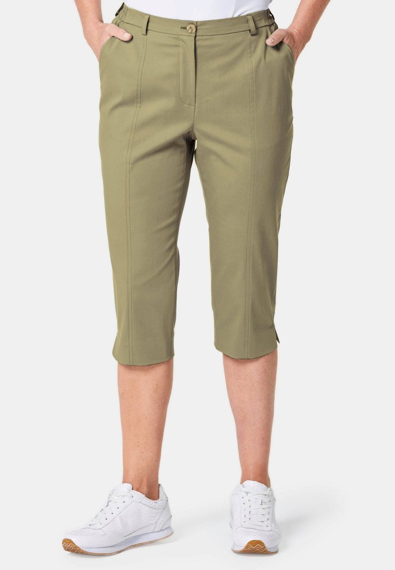 Khakifarbene Capri-Hosen mit taillierter Passform, ausgestattet mit Fronttaschen, dezenten Falten und einer glatten Textur. Kombiniert mit weißen Turnschuhen.