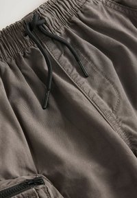Shorts à taille élastique en tissu gris foncé avec une finition texturée. Dotés d'un cordon de serrage ajustable, d'une poche zippée sur le côté et de détails de couture.