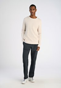 Beige geribd trui, zwarte broeken en witte sneakers. De trui heeft een ronde hals en lange mouwen, met een zachte textuur en een relaxte pasvorm.