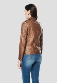 Giacca da motociclista in pelle marrone con pannelli testurizzati sulle spalle, dettagli con cerniere e design aderente, indossata sopra jeans blu.