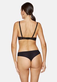 Czarny komplet bielizny z transparentnym biustonoszem z tyłu, z regulowanymi ramiączkami i zapięciem oraz dopasowanymi majtkami typu low-rise wykonanymi z podobnego materiału.