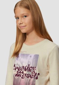 Hellbeige Langarmshirt mit großem Grafikdruck, auf dem in fettem Burgunderrot der Text "Creating Myself" zu sehen ist. Weicher Stoff, Rundhalsausschnitt.