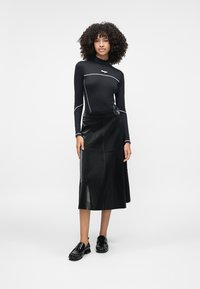 Camisola preta de mangas longas com acabamento cinza, combinada com uma saia midi preta em couro sintético. A saia tem uma textura suave e um detalhe de cinto lateral.