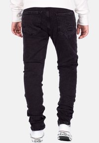 Jeans in denim nero con un design slim fit, caratterizzati da tasche posteriori, logo "RS" impresso e un tessuto leggermente testurizzato. Indossati con sneakers bianche.