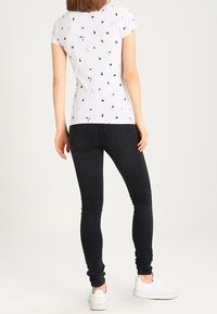 Camisa gris de manga corta con estampados geométricos negros, combinada con unos jeans skinny negros y zapatillas blancas. Vista desde la parte de atrás.