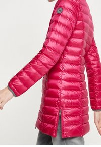 Gewatteerde roze jas met lange mouwen, voorzien van een getailleerd ontwerp, ritssluitingen aan de zakken, zijsplitten en een ronde logopatch op de bovenarm.