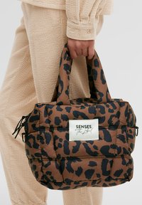 Braune gepolsterte Handtasche mit schwarzem Leopardenmuster, mit zwei kurzen Griffen und einem rechteckigen Etikett mit der Aufschrift "SENSES The Label" auf der Vorderseite.