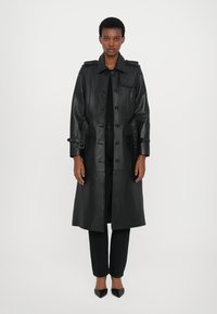 Black leather trench coat with a belted waist, buttons, and two side pockets. Features a classic collar and slightly tailored fit.