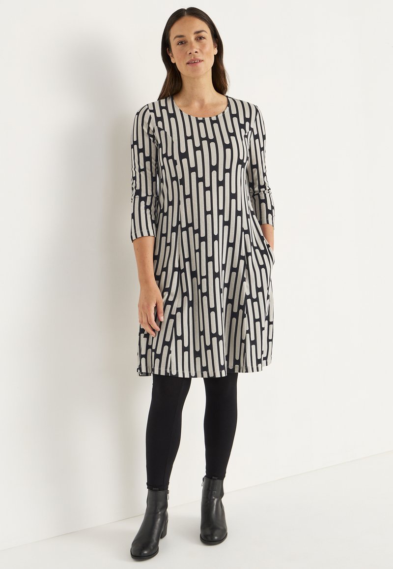 Svartvitt mönstrad klänning med trekvartslånga ärmar, utställd form, sidofickor, kombinerad med svarta leggings och stövletter.