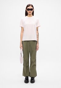 Ανοιχτό ροζ βαμβακερό μπλουζάκι, χαλαρή εφαρμογή, κοντά μανίκια. Ελιώσιες πράσινες παντελόνες σε φαρδύ στιλ, λεία υφή. Μαύρες χοντρές μπότες, μικρή ροζ τσάντα.