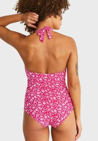 En bikini i ett stycke i rosa blommönster, har en knyt-bak halterneck-design, elastisk tyg och medelhöga benöppningar.