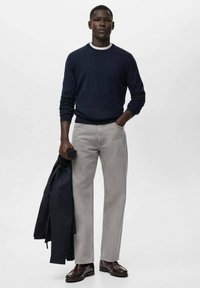 Suéter azul marino, pantalones grises y zapatos oscuros. El suéter es de punto y los pantalones son de mezclilla de pierna recta con costuras visibles.