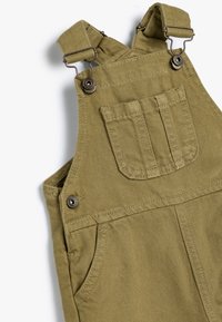 Pantalones de tirantes de algodón verde oliva con correas ajustables, cierres de metal y un bolsillo frontal con detalles cosidos. Tejido duradero con un acabado texturizado.