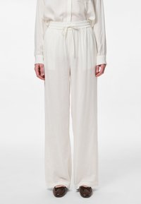 Pantalons larges blancs en tissu léger avec une taille élastique et un cordon de serrage. Texture lisse, sans motifs ni accents visibles.