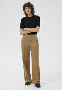Bruine corduroy wijdlopende broek met een gestructureerd oppervlak, voorzien van zijzakken en een hoge taille, gecombineerd met een aansluitend zwart T-shirt met korte mouwen.