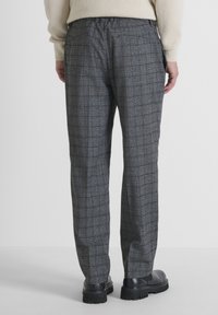 Grijze geruite broek met een relaxte pasvorm, gemaakt van een gestructureerde stof, met een elastische tailleband en taps toelopende benen. Zwarte schoenen maken de look compleet.