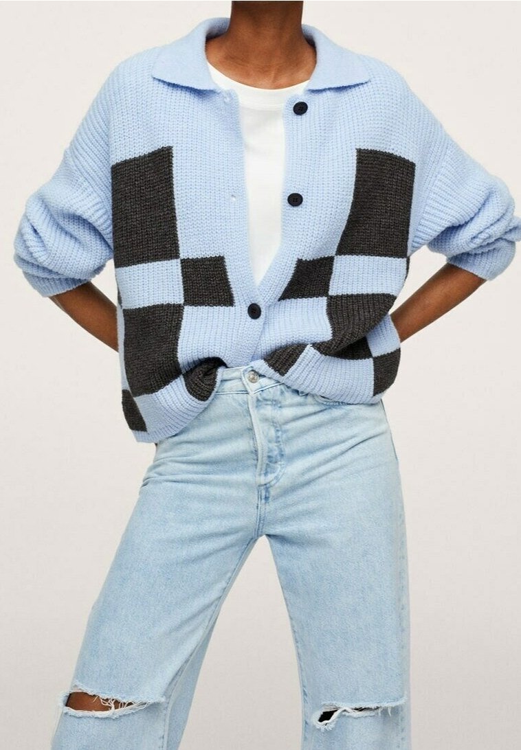 Cárdigan de punto azul claro con patrón de bloques gris oscuro, cierre de botones y textura suave. Combinado con jeans rasgados azul claro.