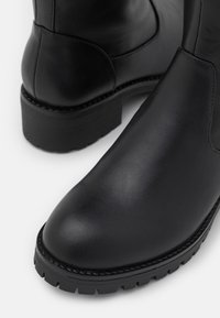 Black leather ankle boots with a structured design. Features a round toe, textured upper, and a rugged sole with visible tread pattern.