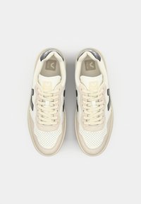 White leather sneakers with beige accents, perforated toe, flat laces, and black logo. Smooth and textured materials with a rounded shape.