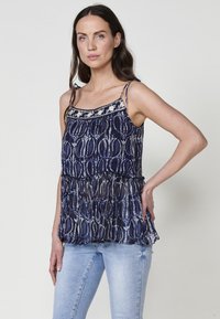 Marineblauwe blouse met een bloemenpatroon bovenkant, kantafwerking en verstelbare bandjes. Gelaagd, tiered ontwerp in lichtgewicht, zwierige stof.