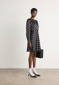 Abito nero con pois bianchi, maniche lunghe e gonna svasata. Abbinato a calzini bianchi e scarpe con tacco a punta nere. Borsa nera.