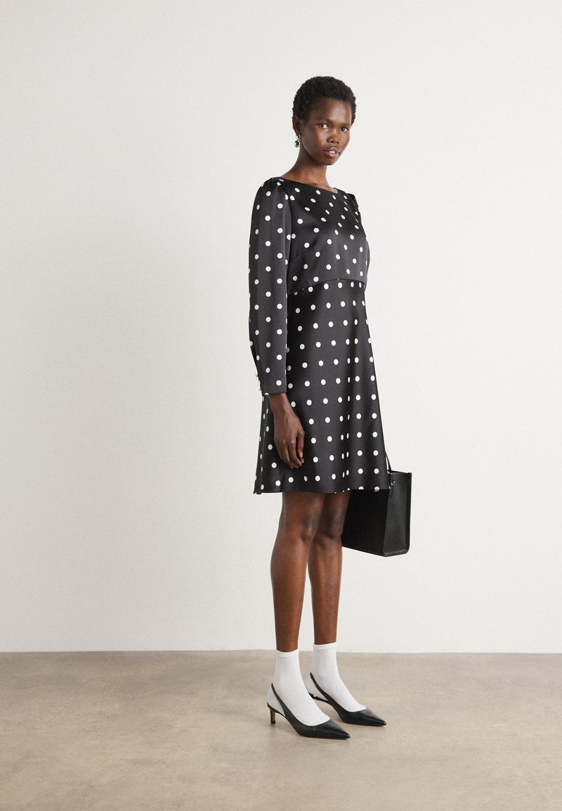 Abito nero con pois bianchi, maniche lunghe e gonna svasata. Abbinato a calzini bianchi e scarpe con tacco a punta nere. Borsa nera.