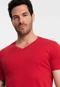 Rød v-hals t-shirt lavet af et glat, strækbart stof, tætsiddende design, kortærmet, med et minimalistisk, ensfarvet mønster.