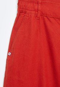 Pantalones de algodón rojos con cinturilla elástica, bolsillo lateral y una pequeña etiqueta con un detalle de estrella cerca de la cinturilla.
